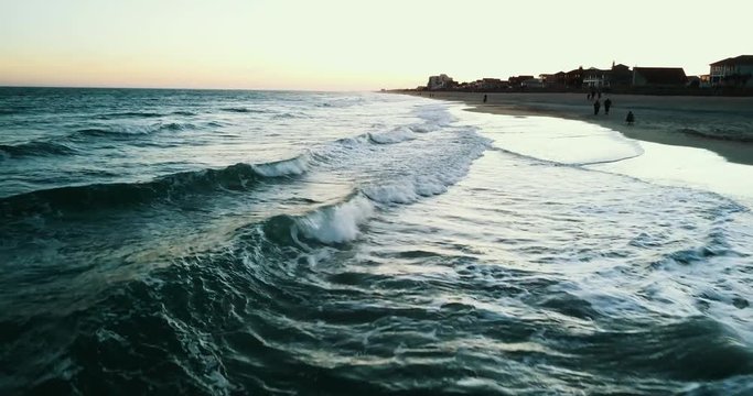 Waves crash on shore at sunset, aerial