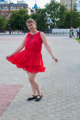 The Russian woman in a red dress walks and has fun in the park in the summer