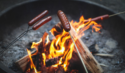 hotdogs roasting on sticks over flames in a campfire - obrazy, fototapety, plakaty