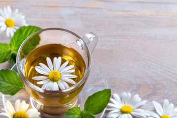 Cup of tea with chamomile flowers and leaves of mint on rustic wooden background with copy space....