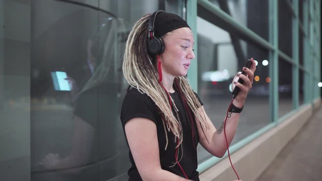 Young beautiful woman with dreadlocks using a smartphone outdoors at night