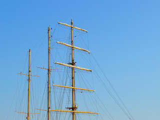 Three masts of a sailing ship with folded up sails and shrouds against a blue summer sky, copy space