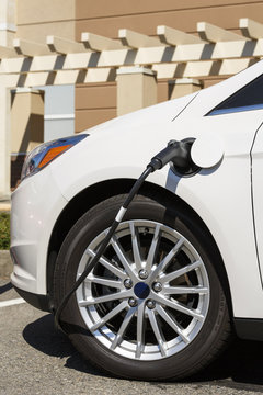 Close-up of electric car vehicle auto in parking lot with cable connected to electrical charging station