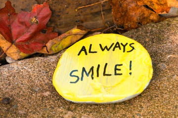 A yellow hand painted flat stone with words 'always smile!'