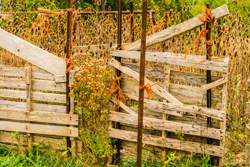 Old make shift retaining fence in rural farm field held together with rope and metal posts.