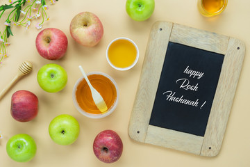 Table top view aerial image of decorations Jewish holiday the Rosh Hashana background concept.Flat lay apple & honey bee cup and wood spoon on modern  yellow paper.Text design season on blackboard.