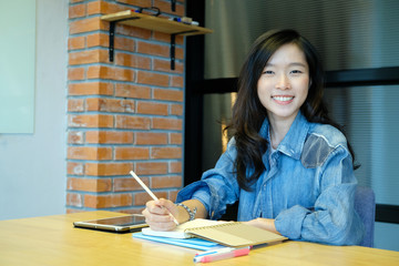 Young asia woman writting on notebook at desk in room with smiling face in happy emotion, education, business, office life, working from home concept