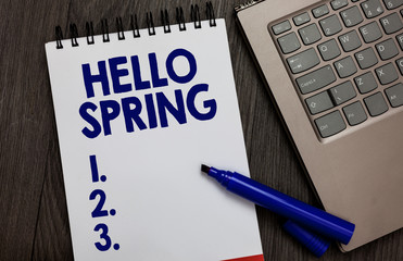 Handwriting text Hello Spring. Concept meaning Welcoming the season after the winter Blossoming of flowers Open notebook white page black marker computer keyboard wooden background