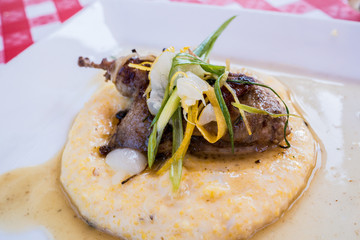 Gourmet cuisine of chicken or quail served on a white plate with a classic checkered table cloth.