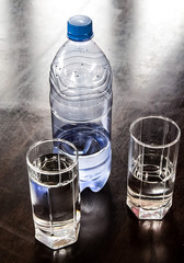 A bottle and two glasses of cold water on a table
