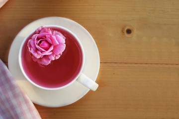 pink rose in tea cup on wood table background in morning light