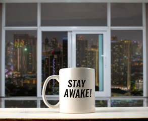Stay awake text on mug with night city view from windows