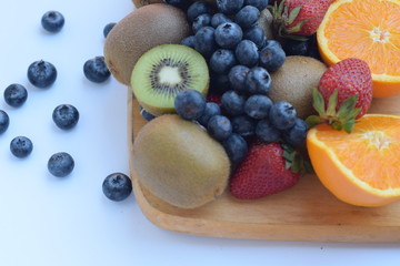 mixed fruit on wood cut board white background isolated,kiwi,blueberry, strawberry, navel orange