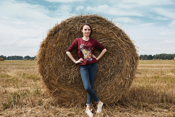 young girl having fun in the field, mowed hay wrapped in a haystack