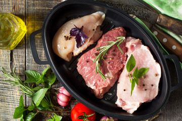 Fresh raw meat. Different types of raw pork meat, chicken fillet and beef with vegetables and herbs on wooden table. Top view flat lay background.