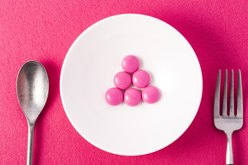 Colorful capsules and pills on plate with fork and knife on white background