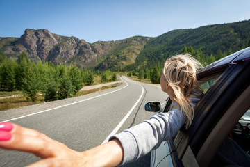 A blonde woman with her head out the window enjoying a scenic drive through the sawtooth mountain. Sun is shining. Shoot from the back