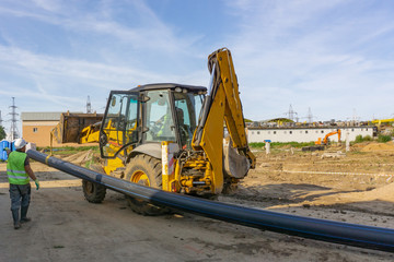 Tractor carries a long pipe for water supply at the construction site