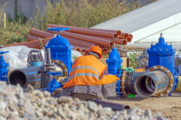 Worker at the construction site assembly elements of the pipeline, plastic pipes, cast iron valve.