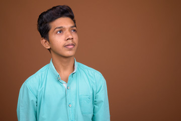 Young Indian boy wearing blue shirt looking smart against brown 