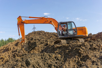 Orange excavator loads the land on a construction site..