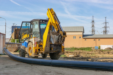 Tractor carries a long pipe for water supply at the construction site