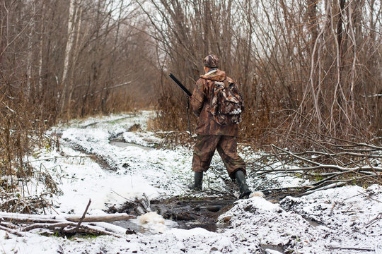 hunter with hunting gun crosses stream in winter