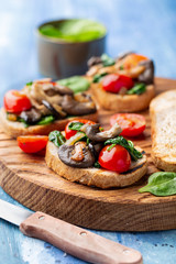 Delicious bruschetta with tomatoes and mushrooms on cutting board on the table 