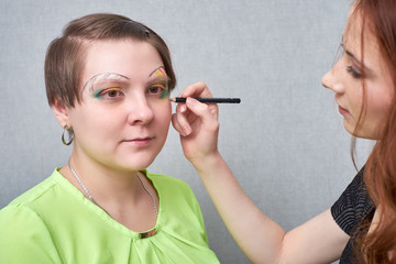 Professional visage artist applying color makeup on woman's face on grey background.