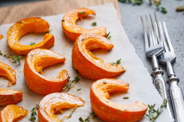 Baked pumpkin slices with thyme on a wooden board over grey table. Seasonal food vegetarian recipe.