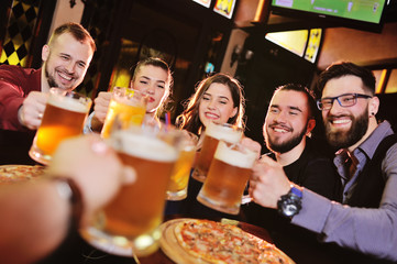 group or company of friends - young guys and girls eat pizza and drink beer in a bar, communicate and laugh.