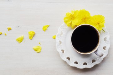 black coffee cup on white heart shape dish with yellow cosmos flower on white wood background  for woman,mother's day,birthday or valentine concept