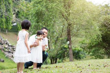Naklejka na ściany i meble Happy Asian family blowing soap bubbles at park