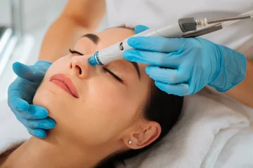 Keuken foto achterwand Schoonheidssalon Facial procedure. Delighted nice woman lying on the medical bed with her eyes closed while having hydrafacial