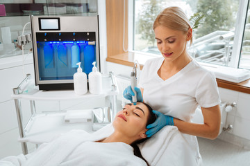 Professional skills. Professional skilled cosmetologist standing near the client while doing...