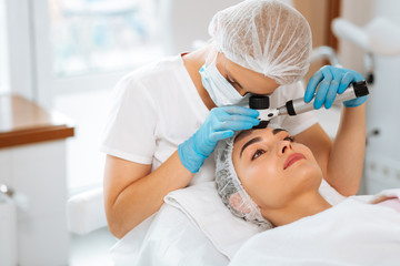 Dermatology clinic. Skilled female dermatologist using a professional dermatoscope while doing the skin examination