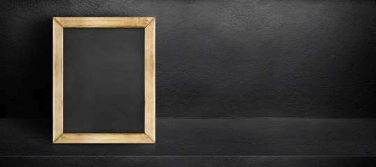 Blank blackboard leaning at black interior cement room background,banner mock up template for display of design,leave side space for adding text for advertising.