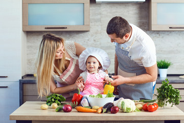 A happy family prepares food from vegetables in the kitchen.