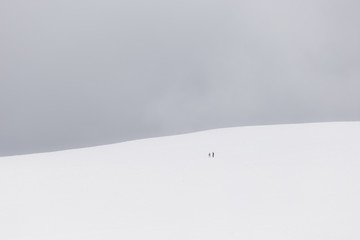 A very minimalistic view of two distant people over a mountain covered by snow