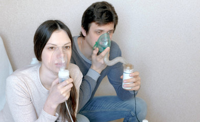 Use nebulizer and inhaler for the treatment. Man and woman inhaling through inhaler mask. Closeup...
