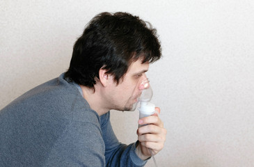 Use nebulizer and inhaler for the treatment. Young man inhaling through inhaler mask. Side view.