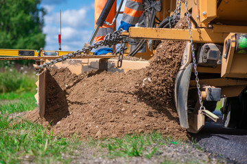 Road construction workers repairing highway road on sunny summer day. Loaders and trucks on newly made asphalt. Heavy machinery working on street. Road curbs being constructed with gravel