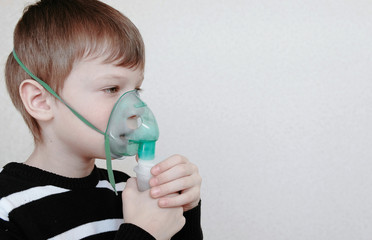 Use nebulizer and inhaler for the treatment. Boy inhaling through inhaler mask. Side view.
