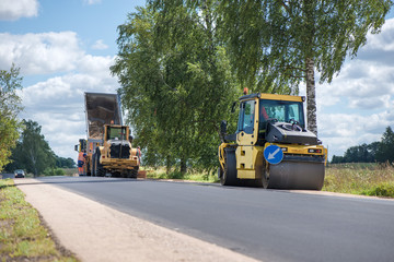 Road construction workers repairing highway road on sunny summer day. Loaders and trucks, heavy vibration roller compactor with arrow road sign on newly made asphalt. Work inspection with drone