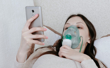 Use nebulizer and inhaler for the treatment. Young woman inhaling through inhaler mask lying on the...