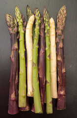 Purple green white asparagus flat lay on black stone background. Vegetarian dieting organic healthy eating concept.