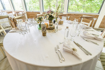 Round wedding table with forest theme, decoration, plates, forks, and glasses.