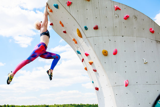 Photo of sporty blonde in leggings hanging on wall for rock climbing against blue sky