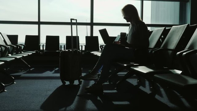 Business woman waiting for her flight at the international airport. She drinks coffee, uses a laptop