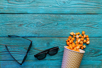 Paper cup with popcorn and 3D glasses on blue background. Top view.